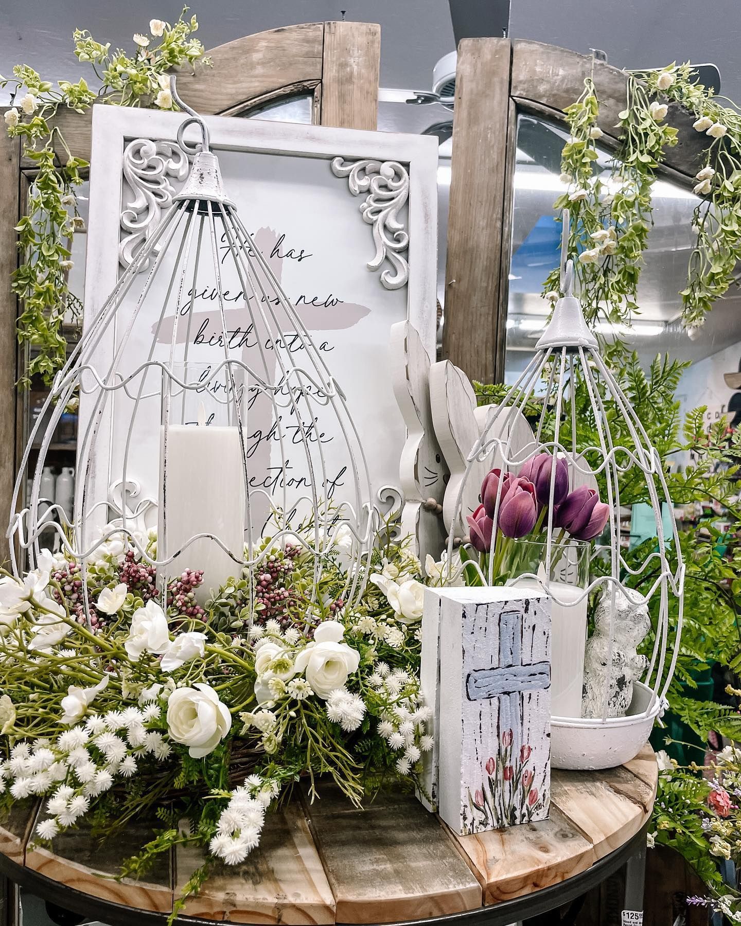 White birdcage decorations with flowers and a candle on a wooden table.