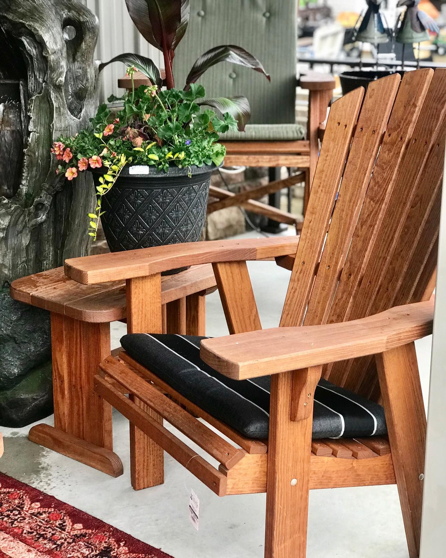 Wooden Adirondack chair with a side table, a potted plant, and a cushion.