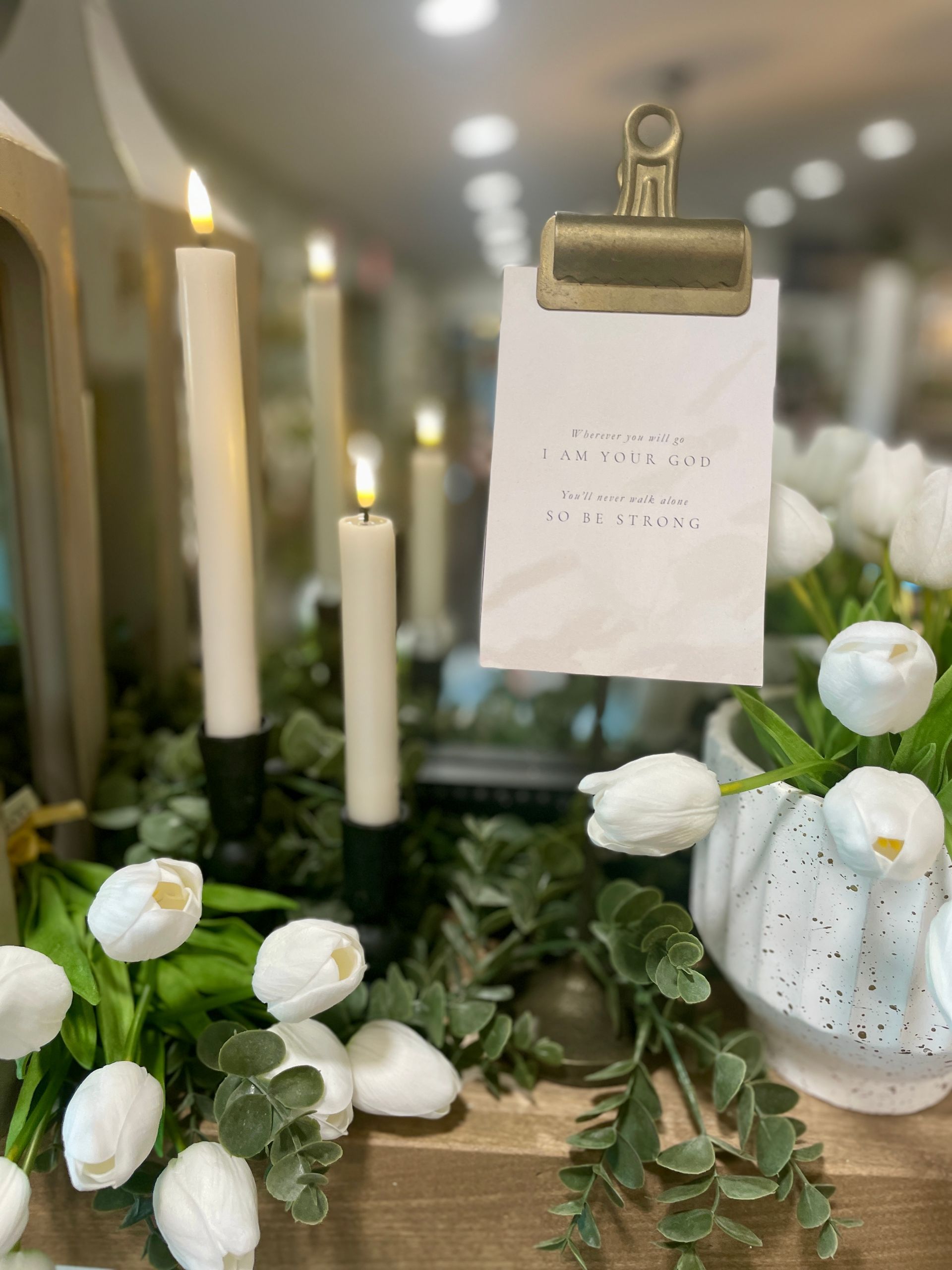 White tulips, faux candles, and a paper-filled clipboard on a decorated wooden surface.