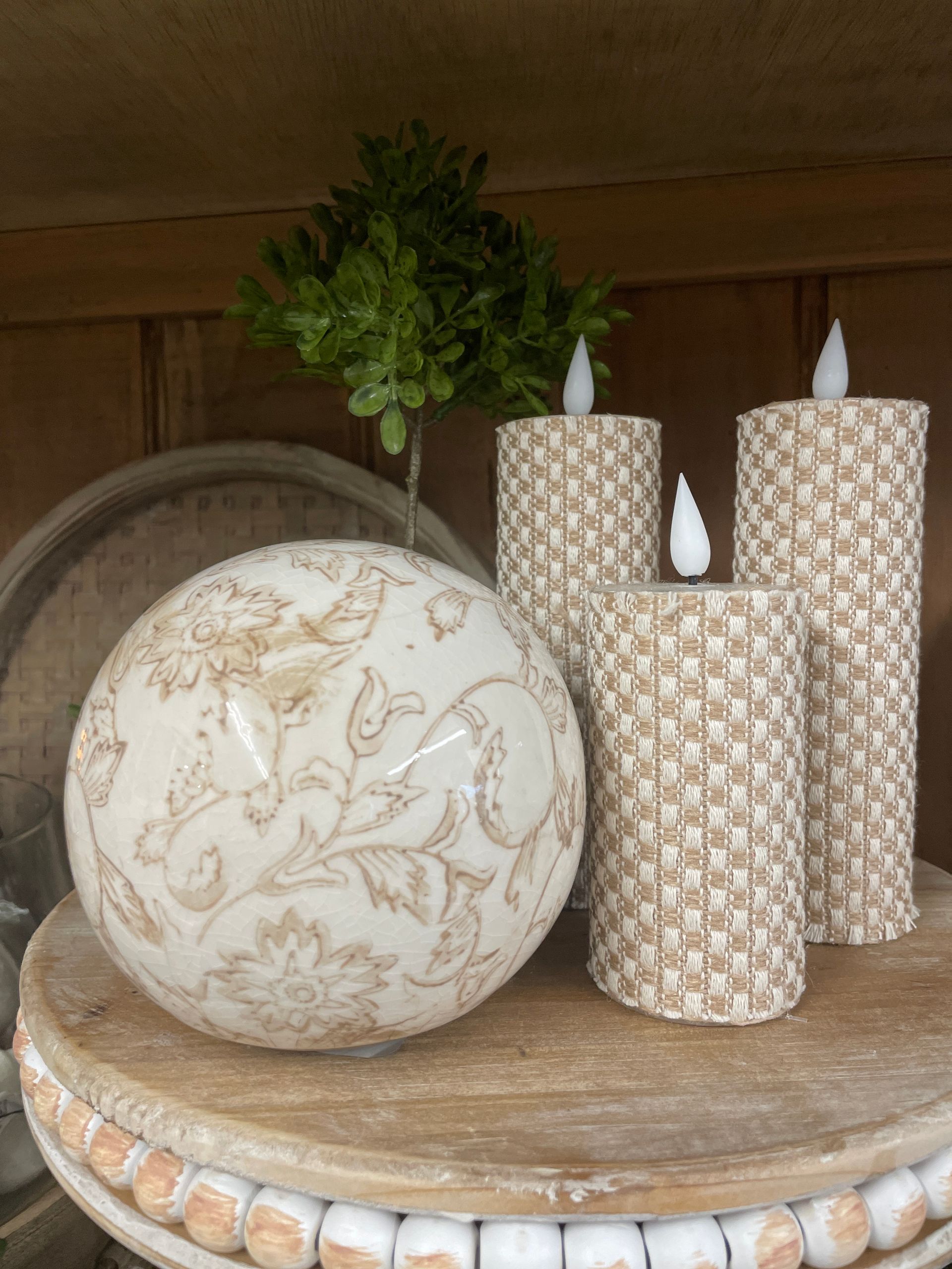 Decorative display: sphere, textured candles, small green plant on a wooden table.
