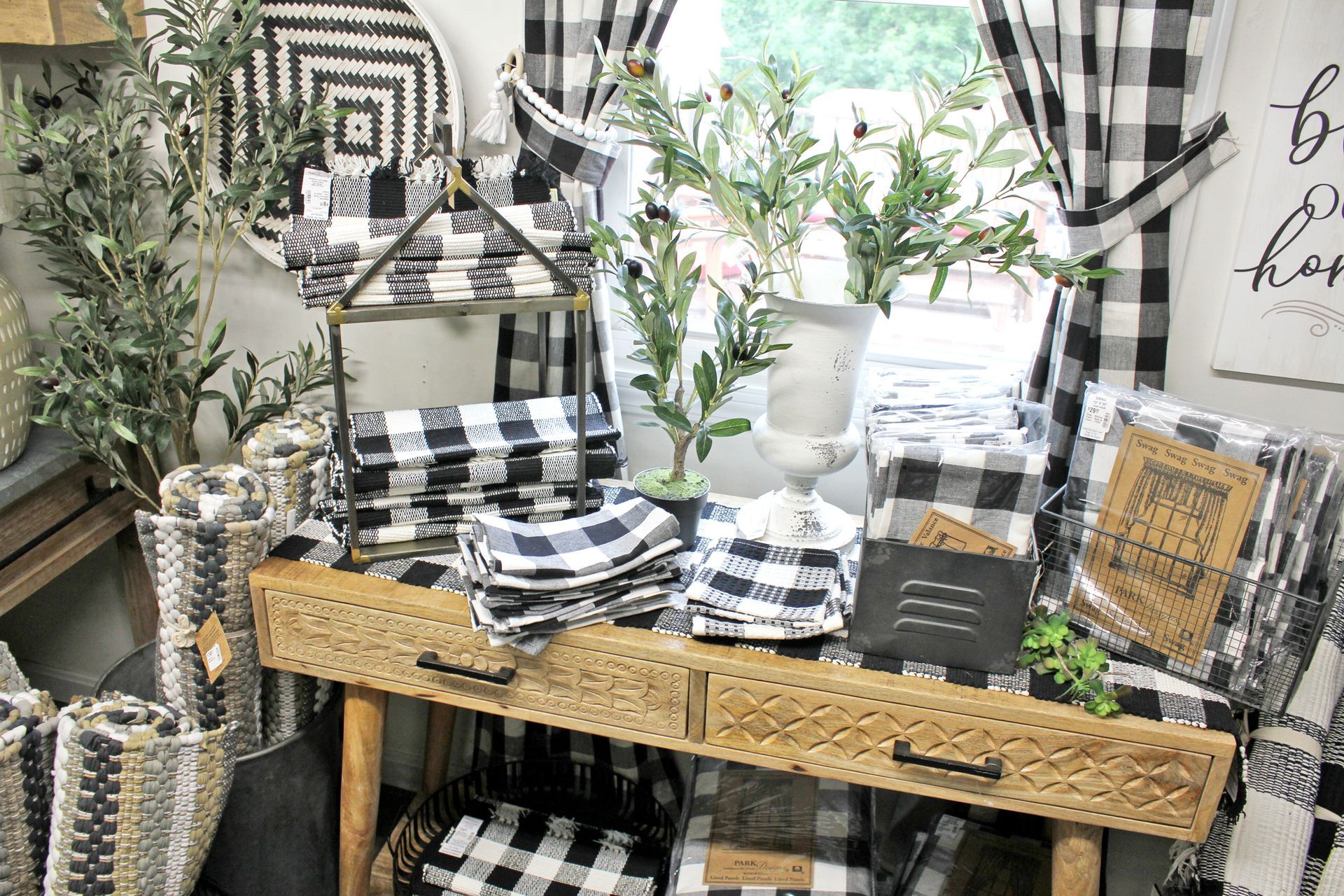 Shop display with black and white checkered textiles, green plants, and wooden table.