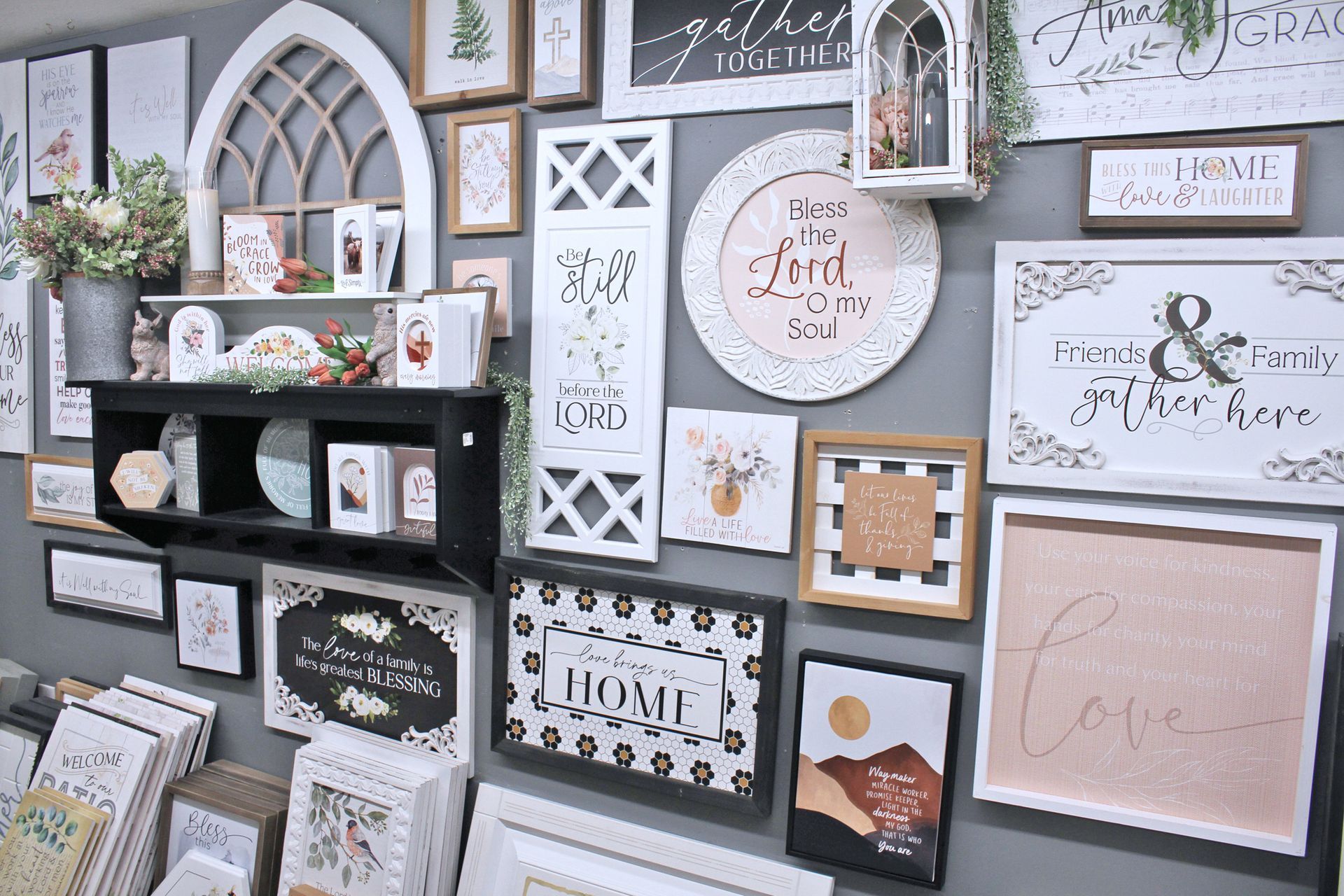 Wall display with framed art, decorative signs, and shelves in a shop; mostly white and black.