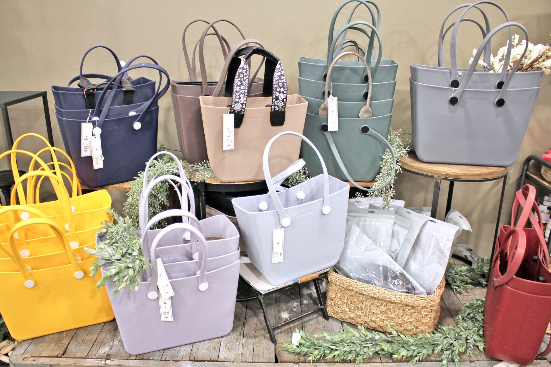 Assortment of colorful tote bags with handle detail, displayed on a wooden surface with greenery.