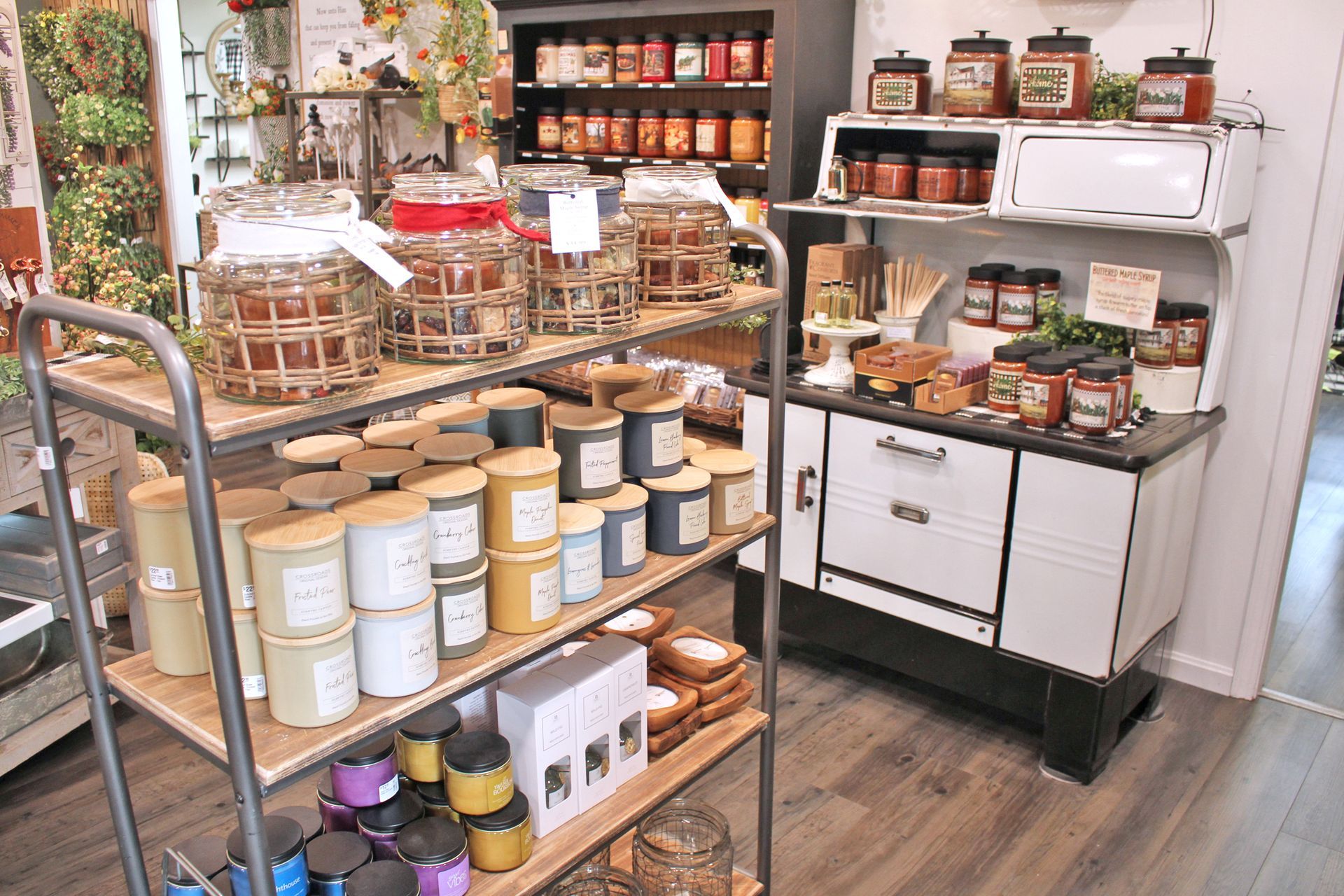 Shop interior with shelves of candles and jars of preserved food. An antique stove displays more jars.
