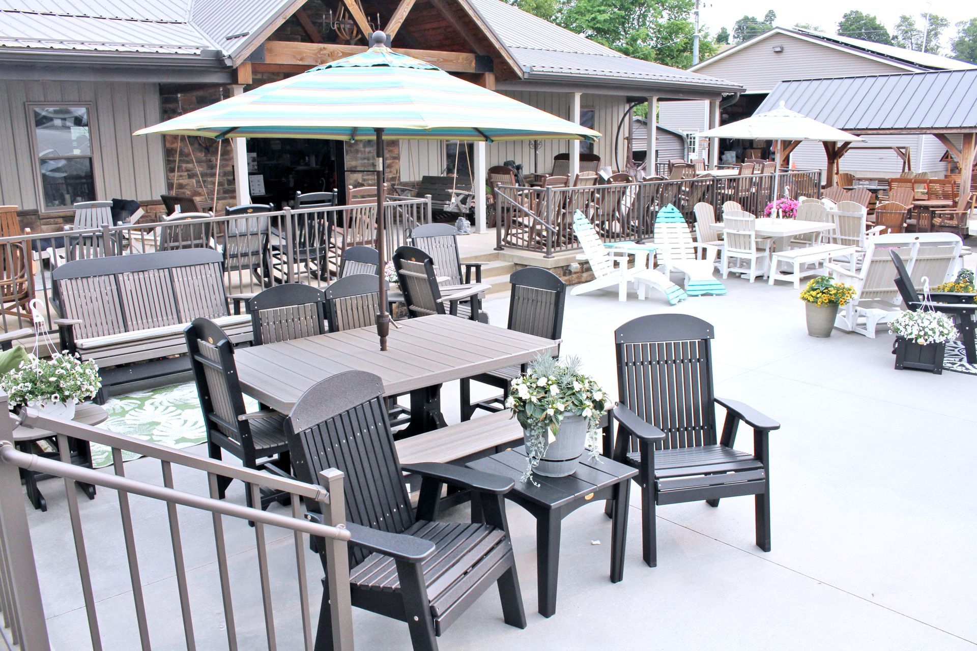 Outdoor furniture display: patio tables, chairs, and umbrellas in front of a building with a rustic design.