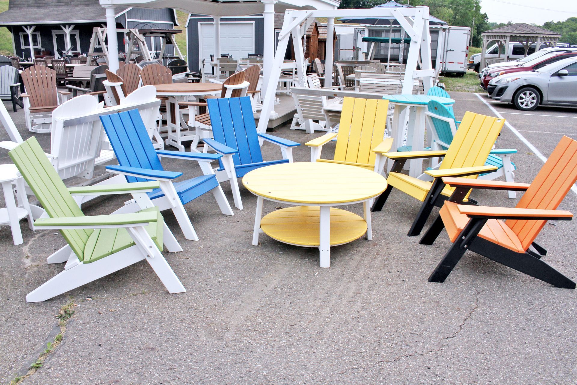 Colorful Adirondack chairs and table display on asphalt in front of a furniture store.