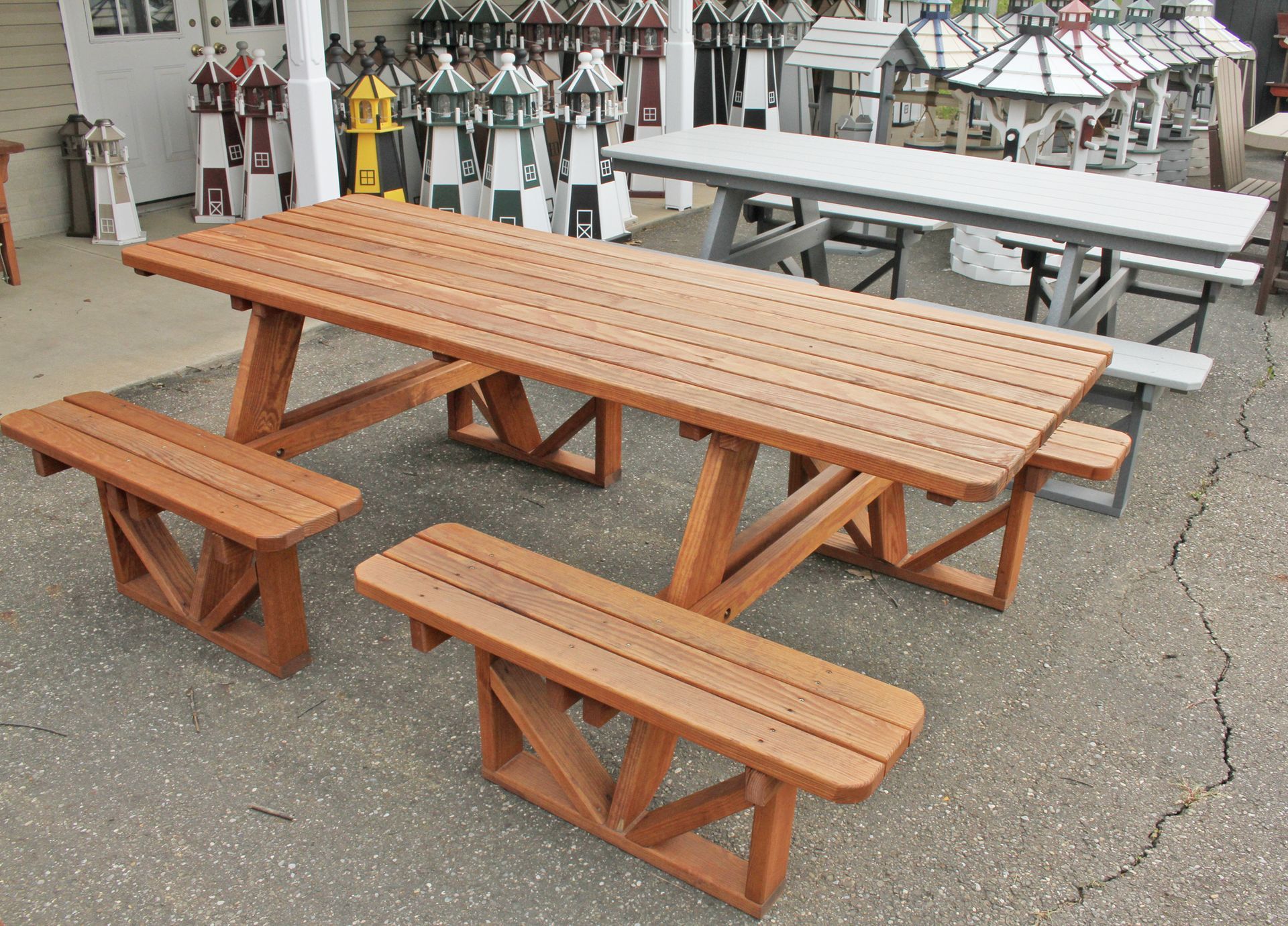 Brown picnic table with two benches, gray picnic table in the background, outdoor setting.