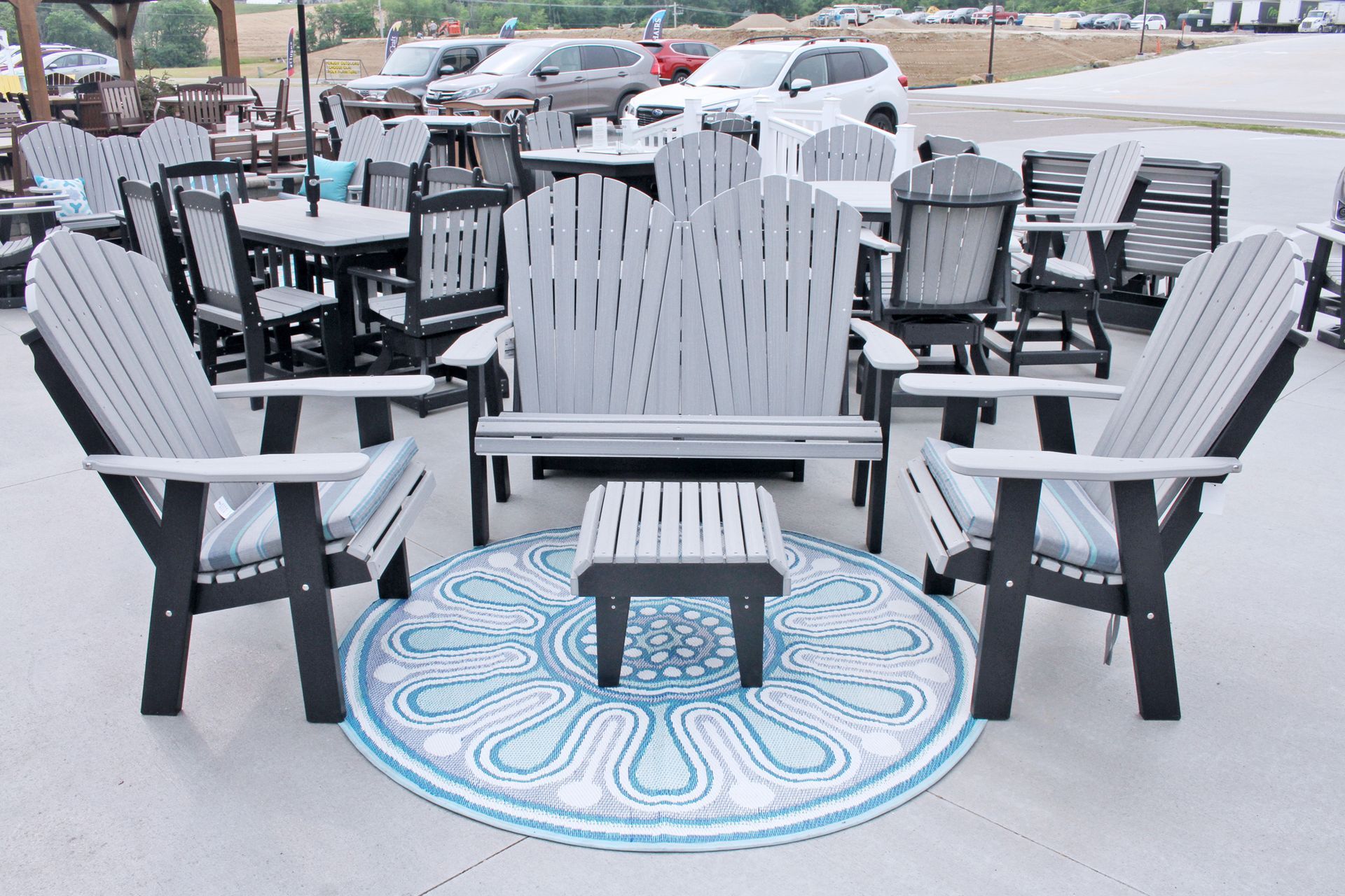 Outdoor furniture set: gray and black chairs, bench, ottoman, on a blue patterned rug, cars in the background.