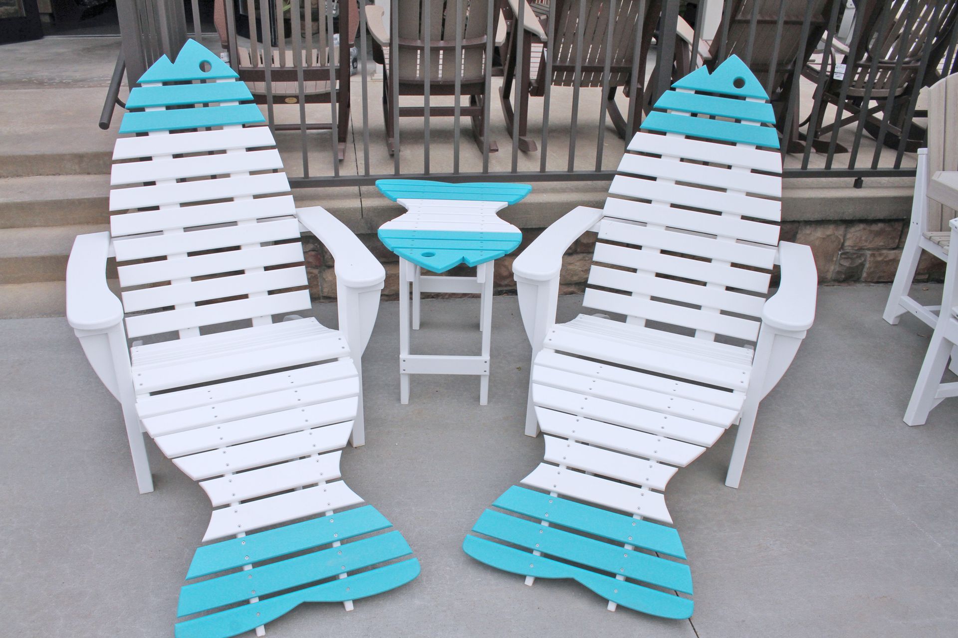 Two white fish-shaped chairs with teal accents flank a matching small table on a patio.