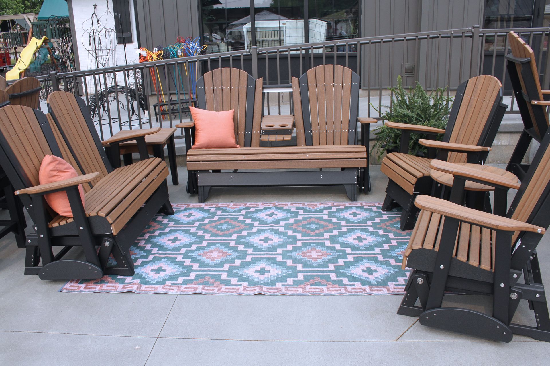 Outdoor seating area with multiple brown and black Adirondack chairs and a rug.