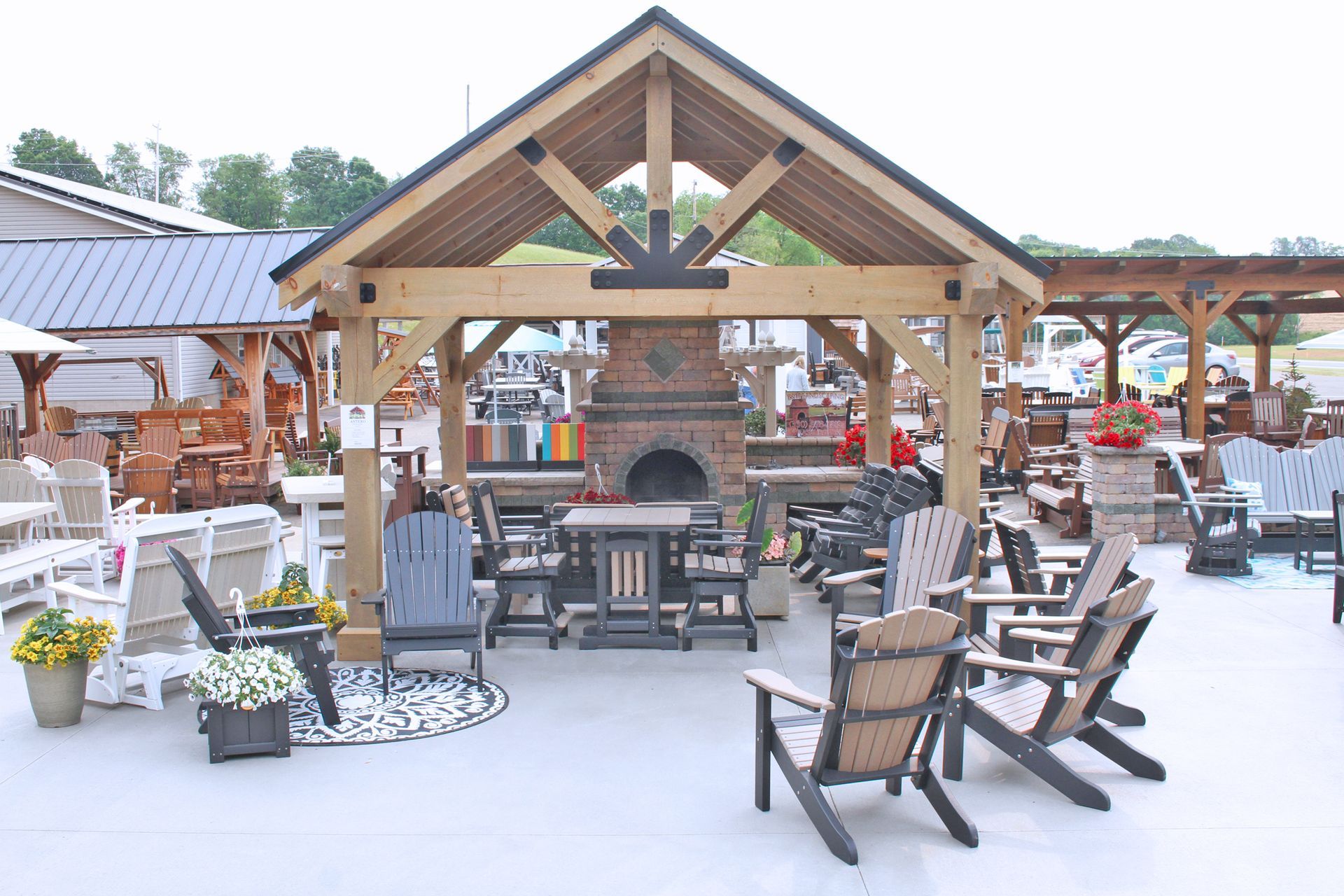 Outdoor furniture display with wooden gazebo, fireplace, and Adirondack chairs.