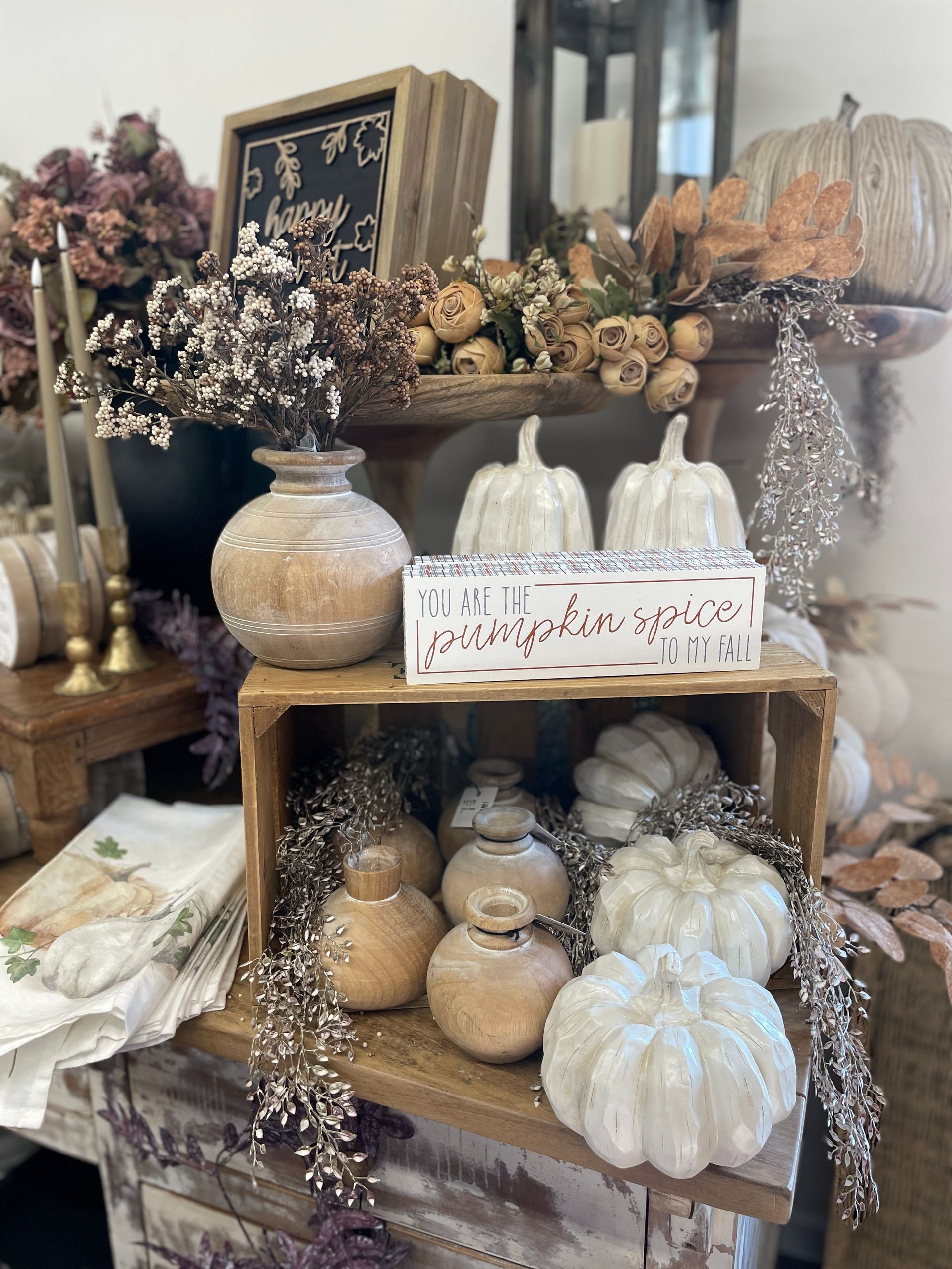 Fall-themed display: white pumpkins, floral arrangements, decorative vases, wooden crate on a table.