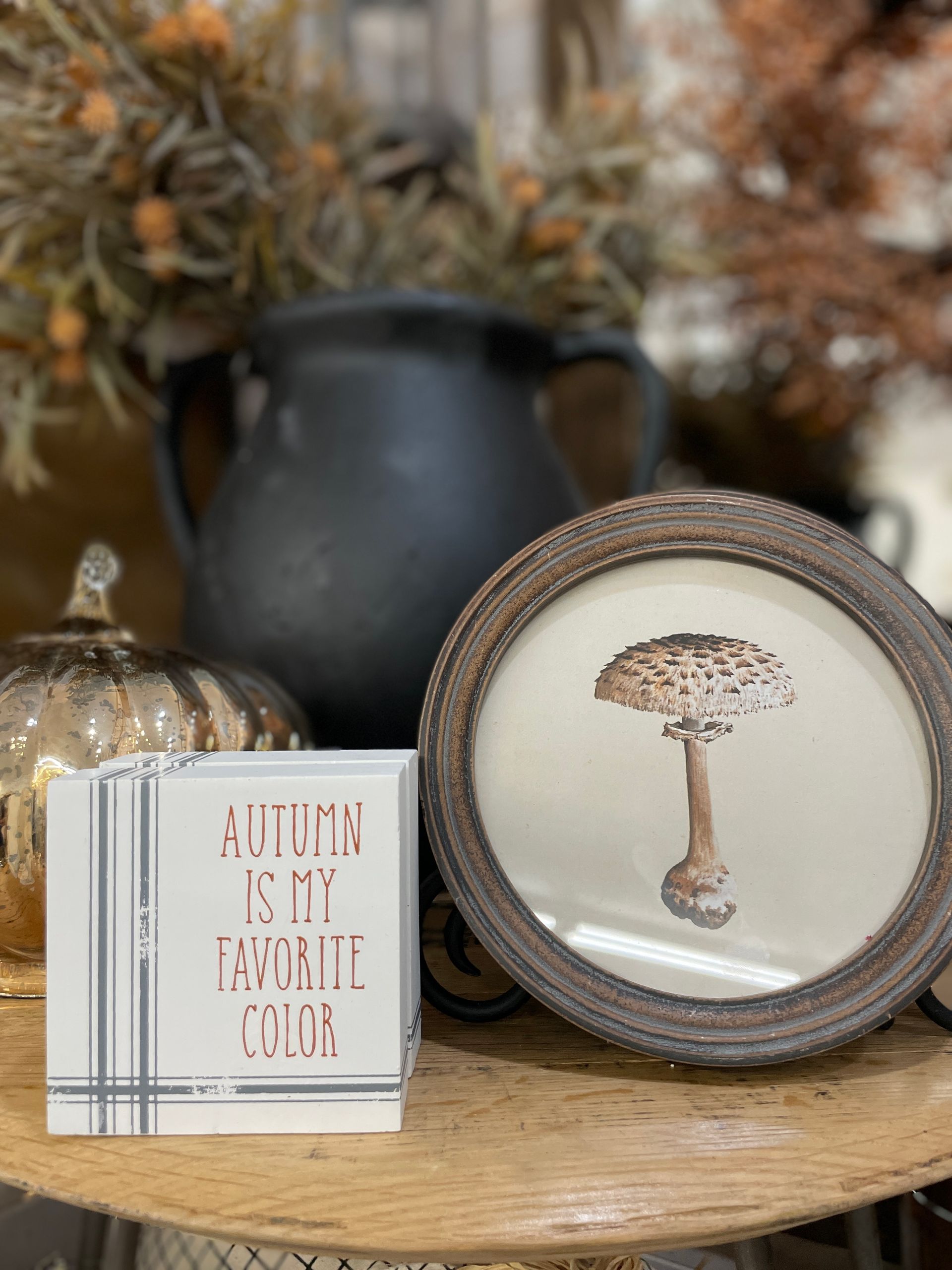 Autumn still life: black pot, framed mushroom art, pumpkin, book stack with text, wood tones.