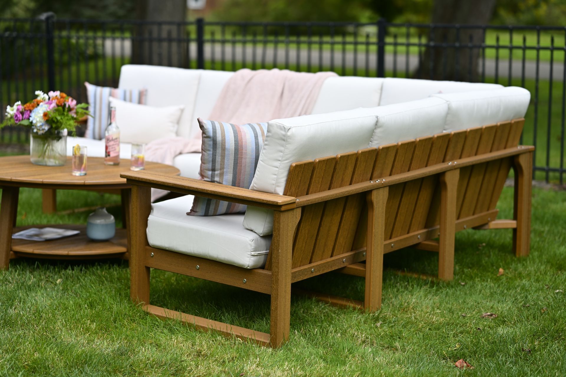 Outdoor sectional sofa with white cushions, a wooden frame, and a round coffee table on a grassy lawn.