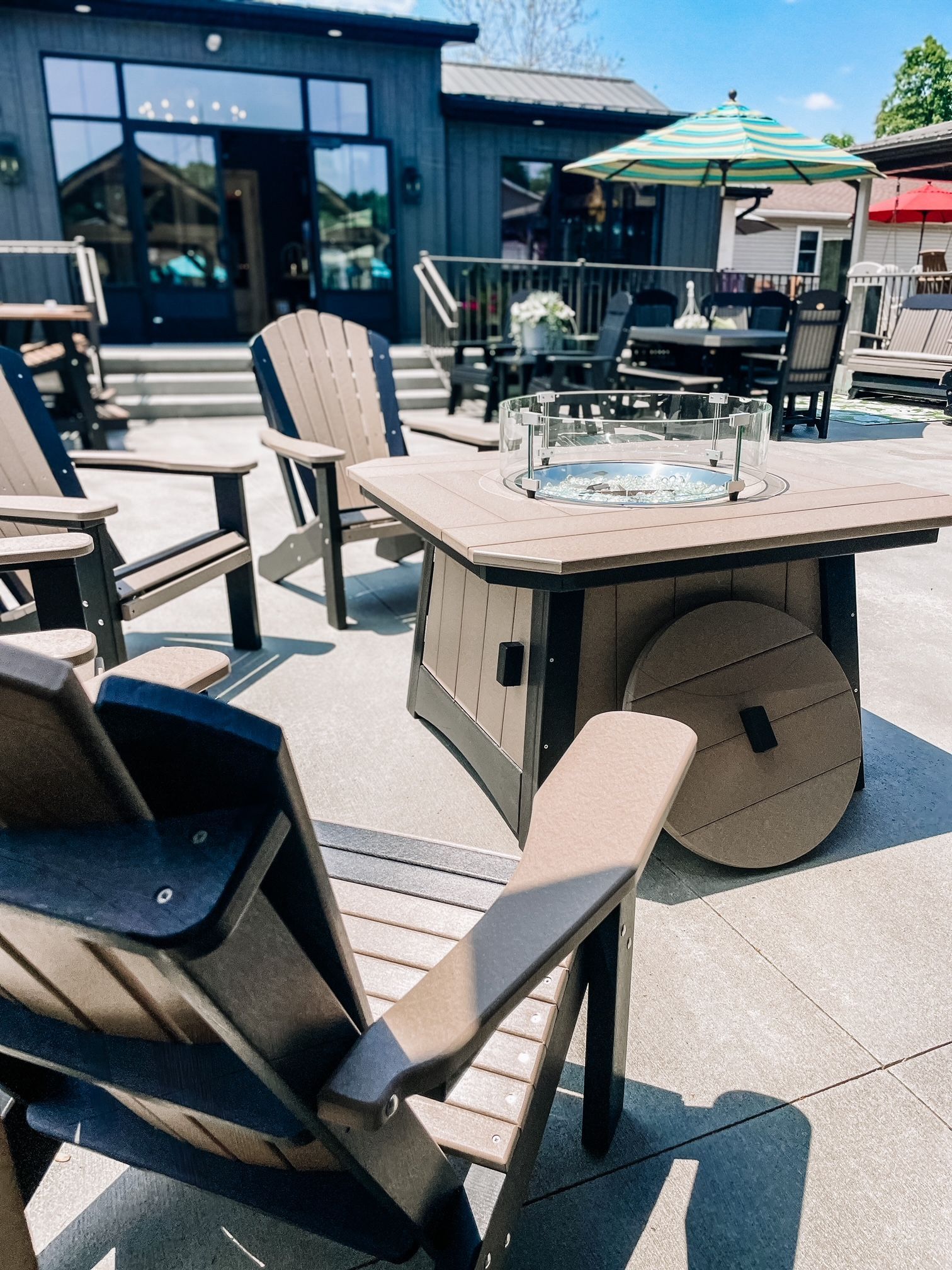 Patio with brown Adirondack chairs, fire pit table, and outdoor dining set near a building.