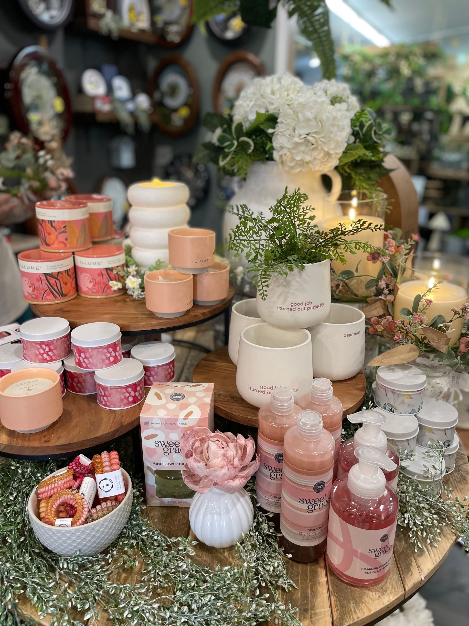 Display of candles, soaps, and flowers in a shop, featuring pink and white colors.