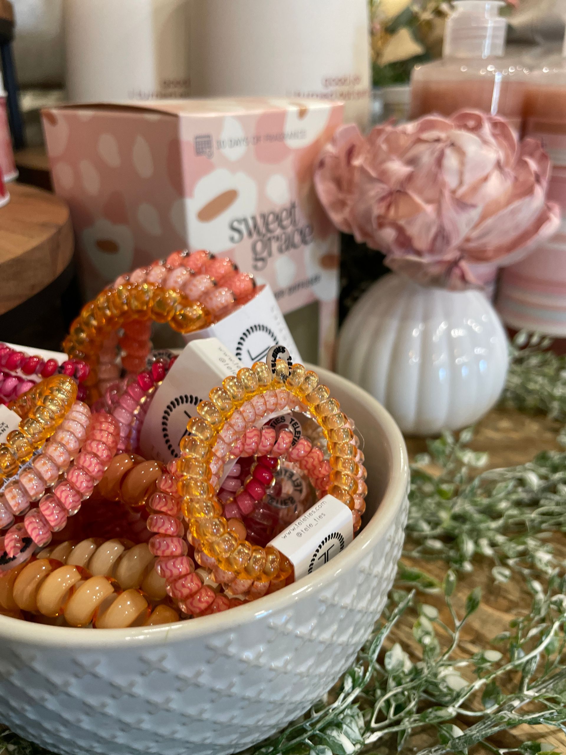 Bowl of colorful spiral hair ties, with pink and orange hues, near a flower and a box of 
