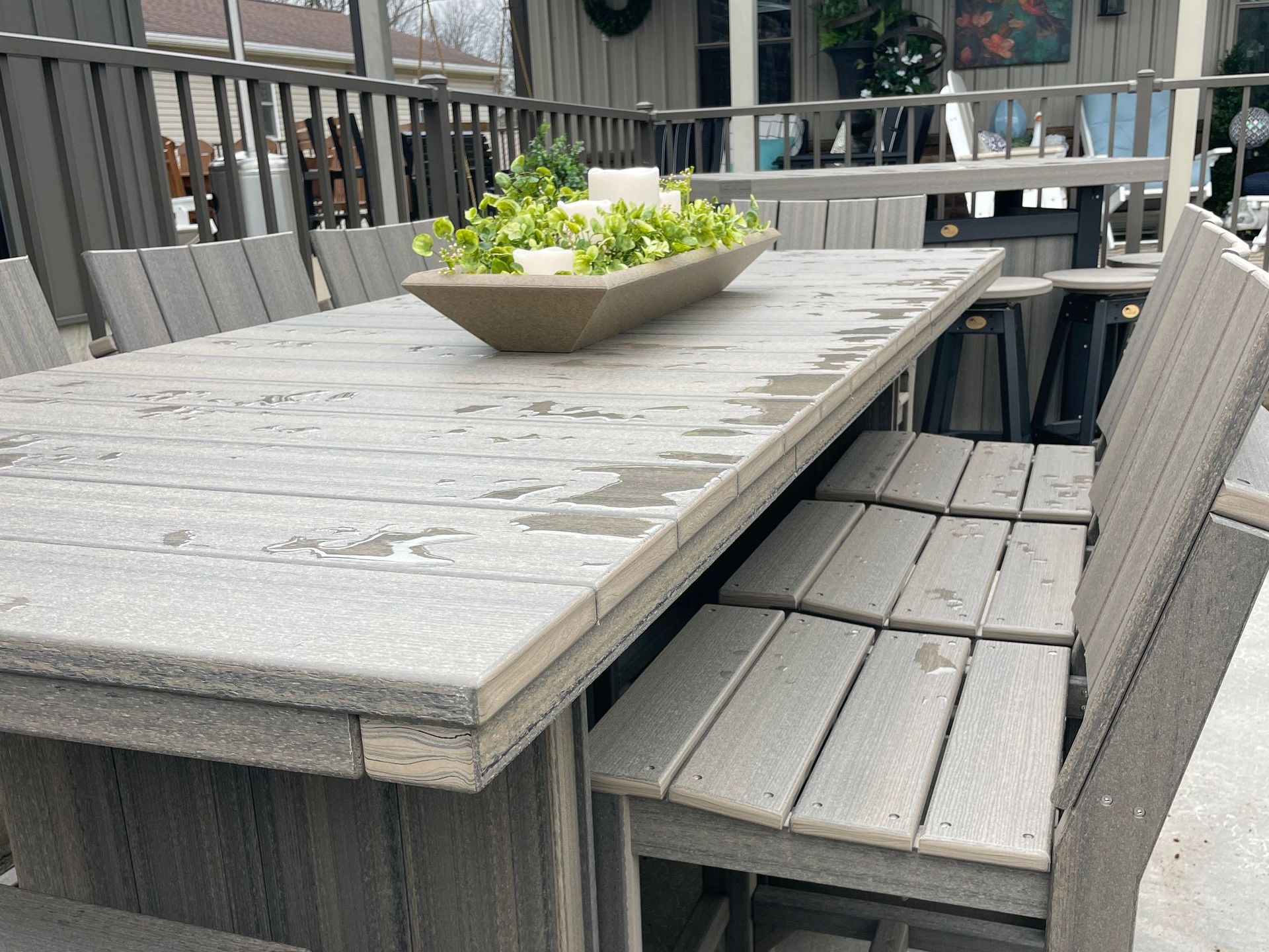 Gray wooden outdoor dining table with matching chairs. A green plant centerpiece adorns the table.