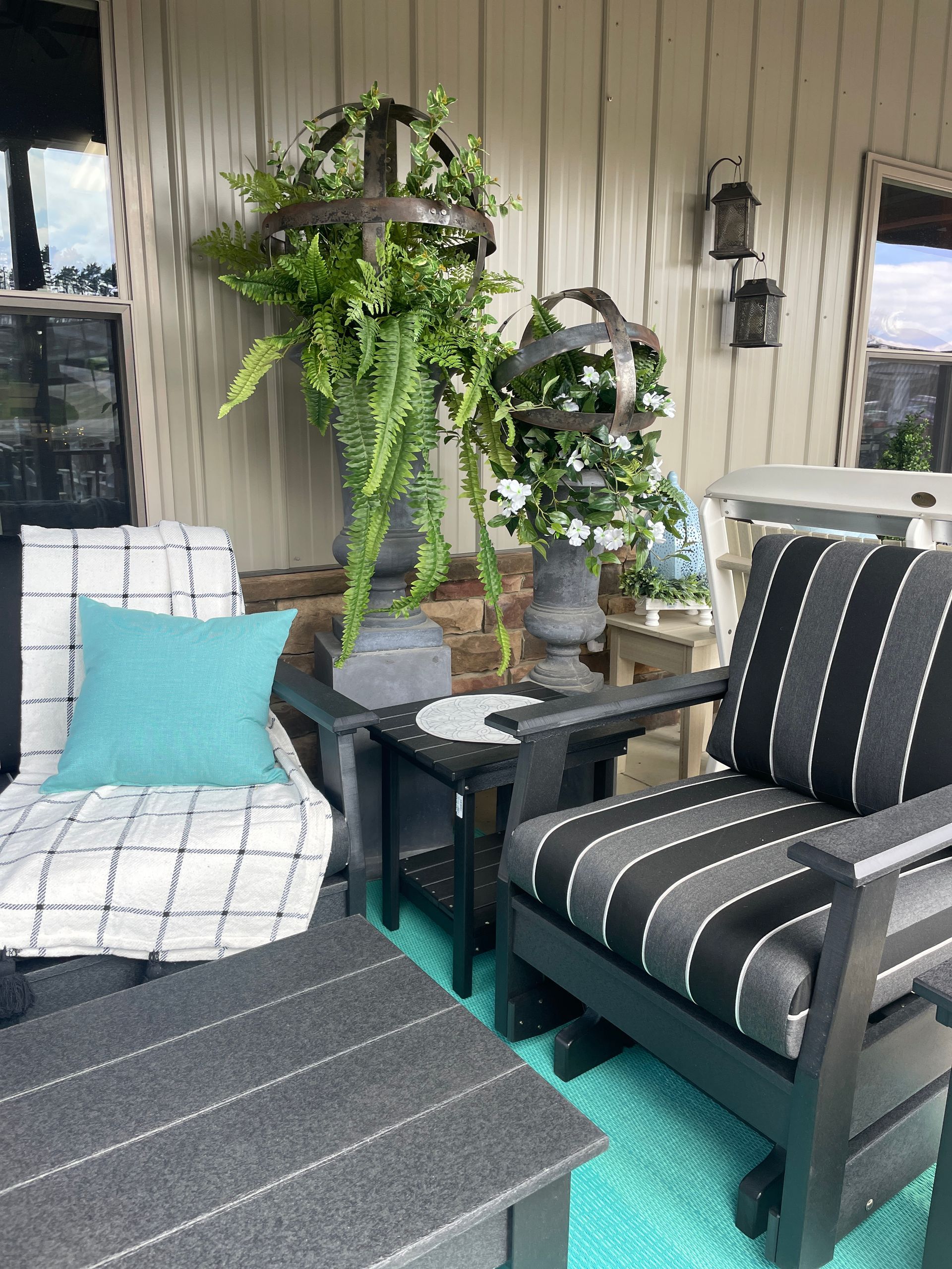Cozy porch seating with black furniture, teal rug, decorative plants, and outdoor lanterns.