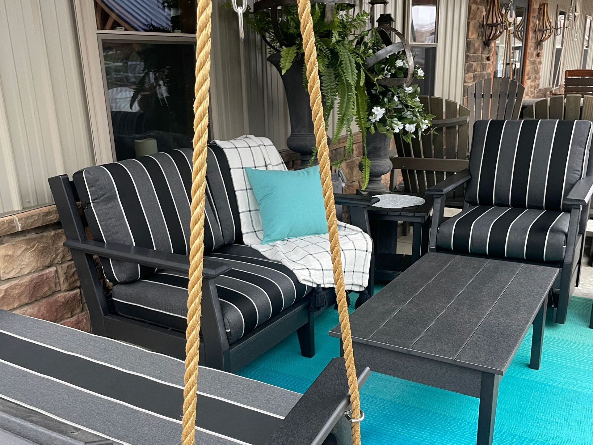 Patio furniture set with black and white striped cushions, teal rug, and hanging swing.