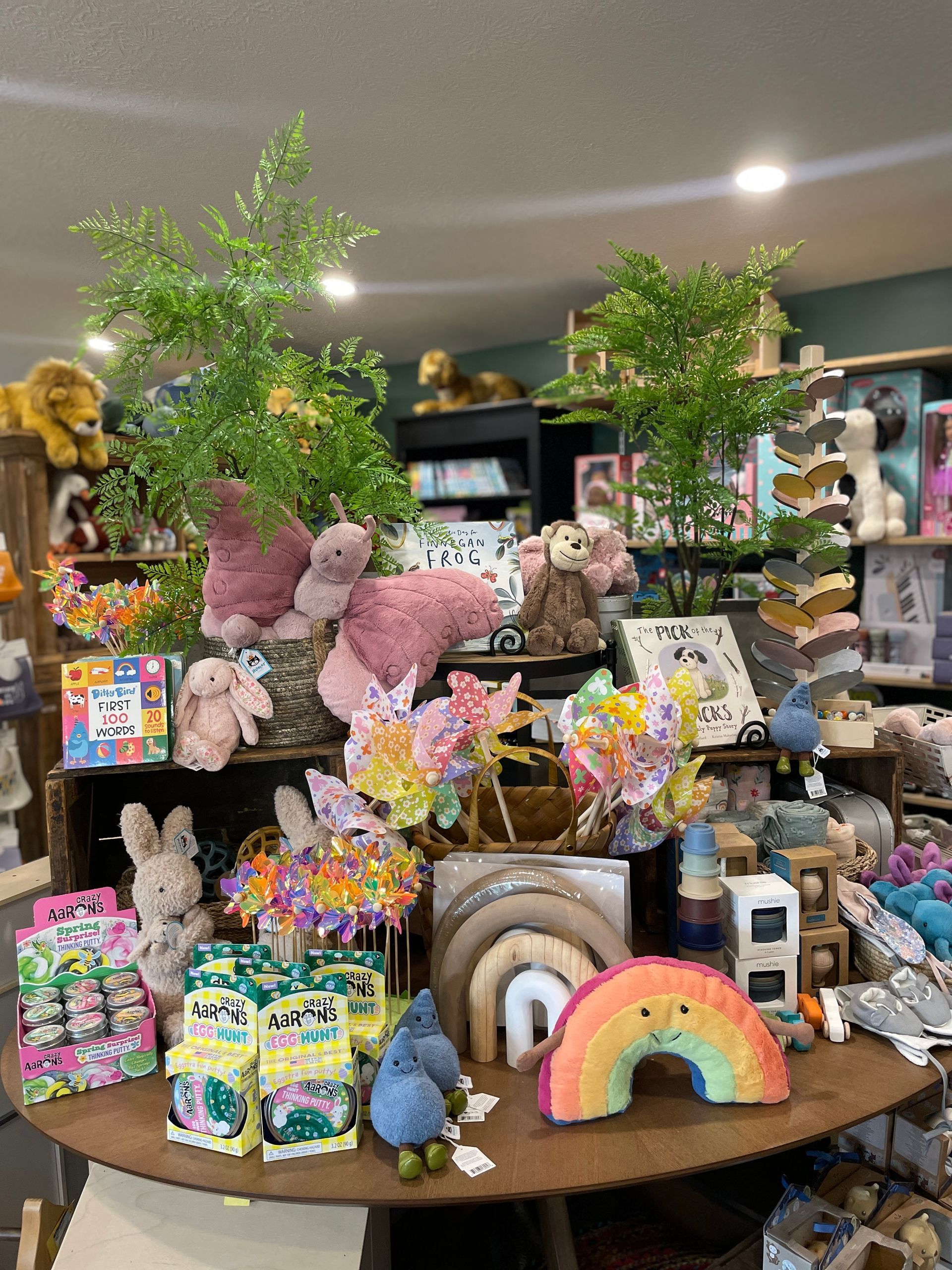 A display table in a store is covered with stuffed toys, colorful decorations, and art supplies.
