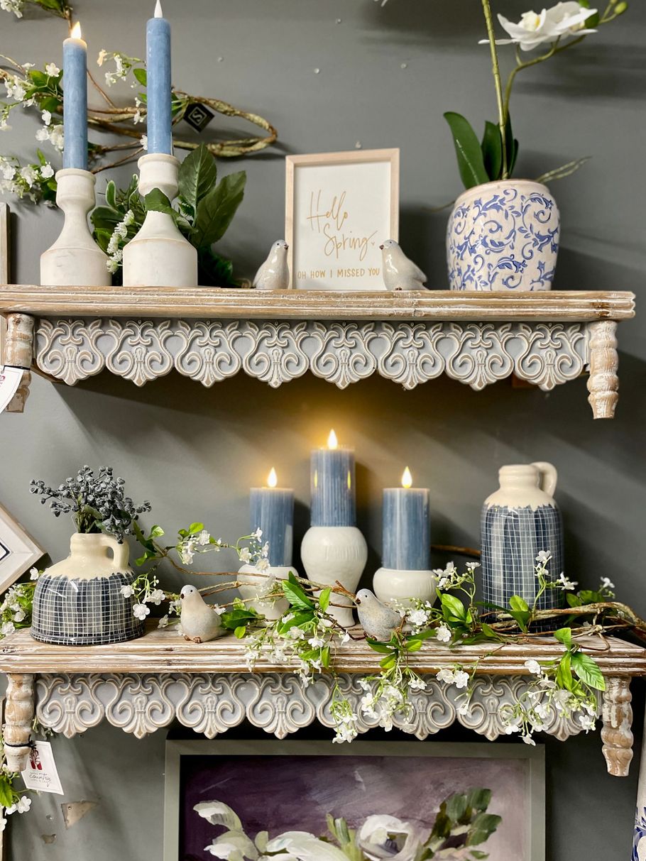 Two shelves decorated with blue candles, greenery, and ceramic decor against a gray wall.