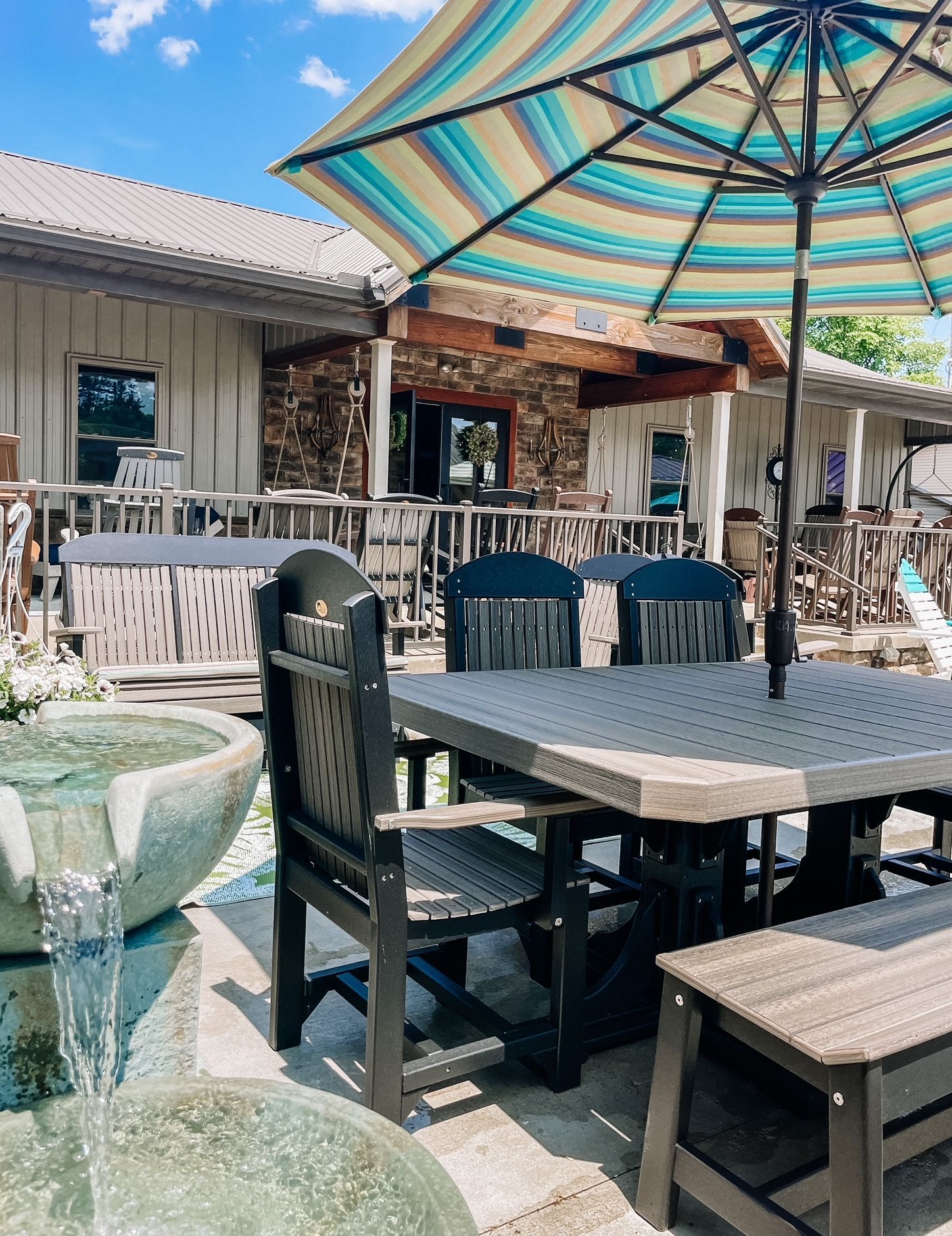 Outdoor dining area with table, chairs, umbrella, fountain, and building in the background.