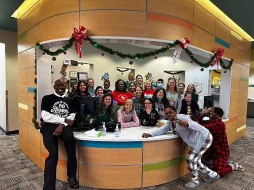 A diverse group of people posing for a photo behind a curved office reception desk decorated with holiday garland.