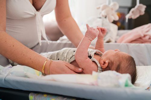 A person in a white top gently tends to a baby lying on a changing pad in a softly lit room.