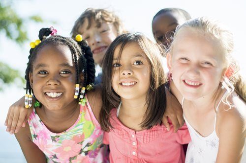 Smiling children posing together outdoors in bright sunlight