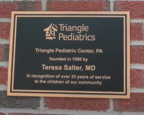 Bronze plaque on a brick wall for Triangle Pediatrics, founded in 1980 by Teresa Salter, MD, honoring 35 years of service.