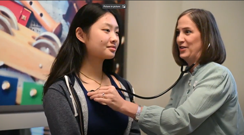 A healthcare provider listens to a patient's heart with a stethoscope in an office setting.