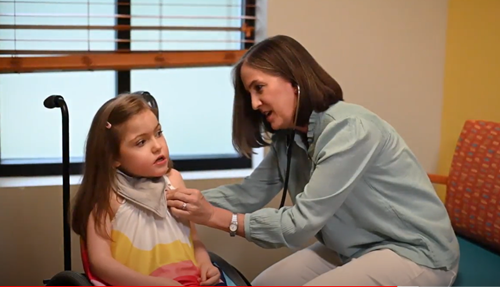 A clinician uses a stethoscope to examine a young patient sitting in a clinical office.