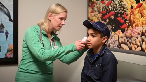 A female pediatrician is looking in the ear of a boy sitting on a medical table.
