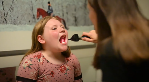 A person uses an otoscope to examine the throat of a patient in a medical setting.