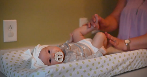 A person changes a baby wearing a white headband and a patterned outfit on a green-spotted changing pad.