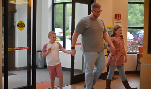 A man holding hands with a boy and a girl as they walk together through a doorway into a building.