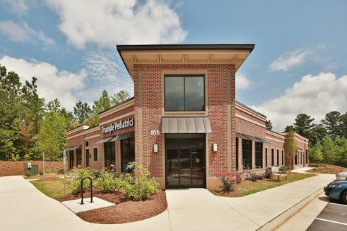 Brick commercial building with large windows, glass entrance, and landscaped front walkway under a cloudy sky