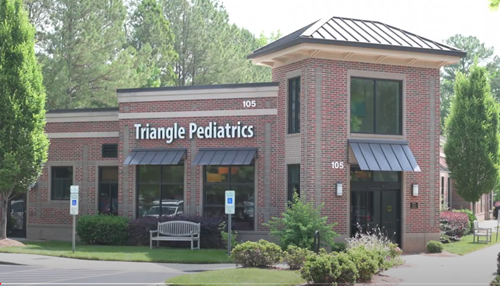 A brick medical office building for Triangle Pediatrics with a metal roof, front entrance, and landscaping.