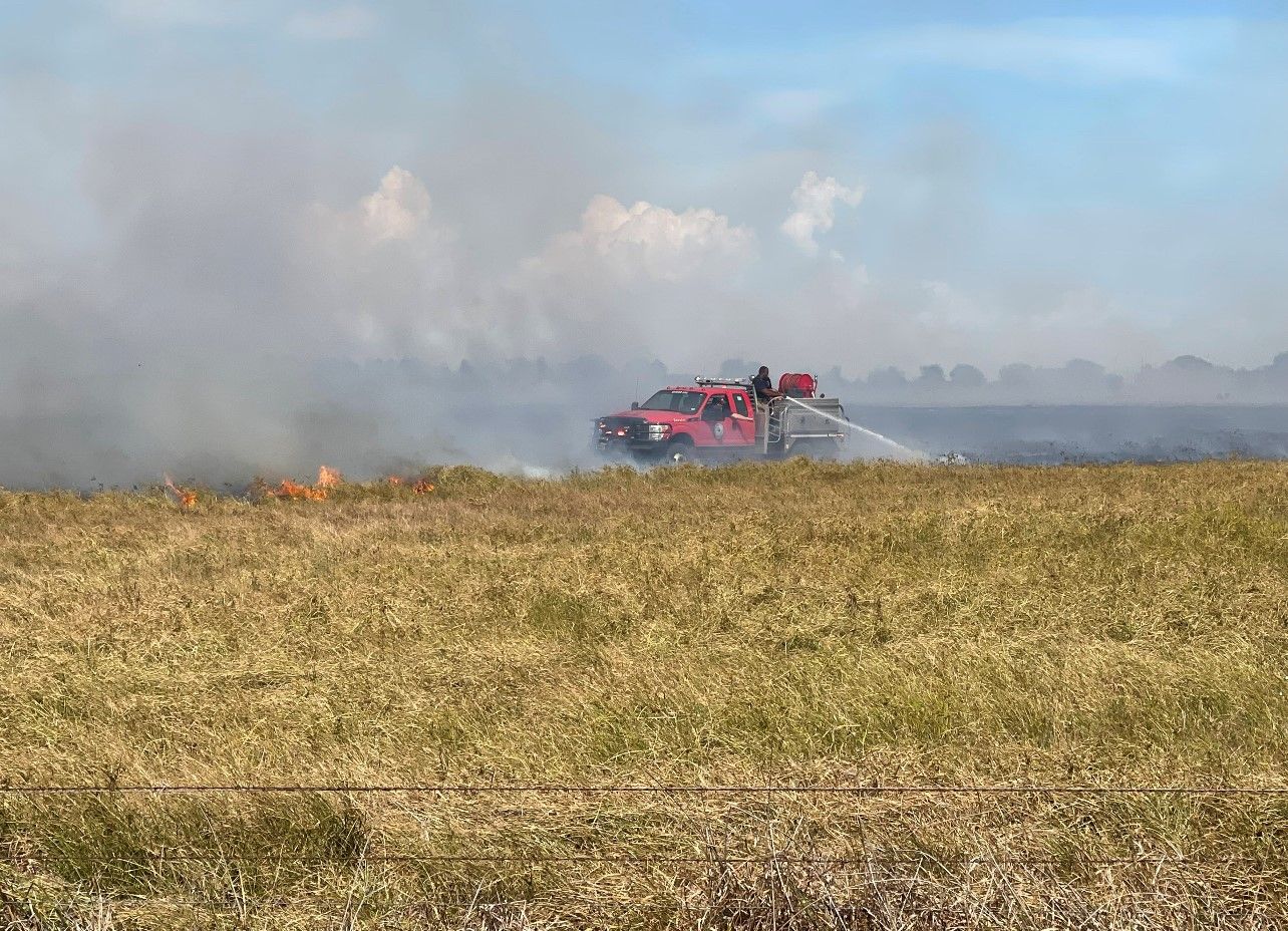 A fire truck is spraying water on a fire in a field.