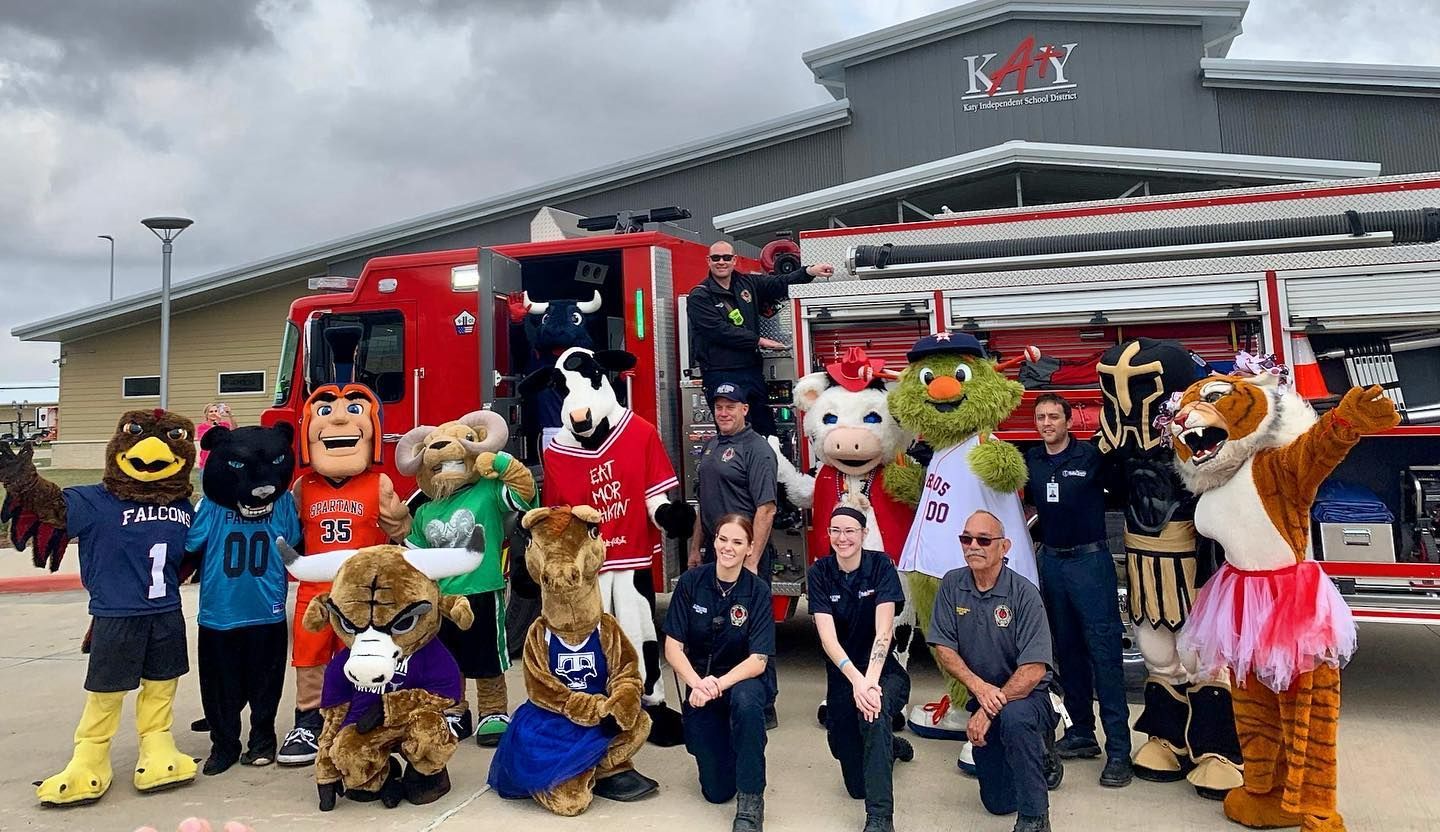 A group of mascots and firefighters are posing for a picture in front of a fire truck.