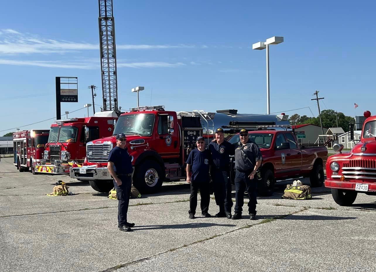 A group of firefighters standing in front of a row of fire trucks