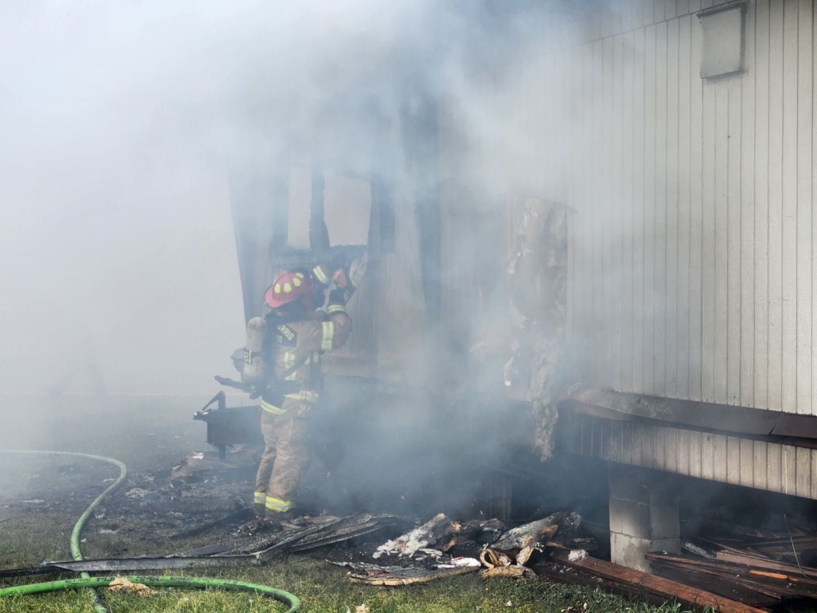 a fire fighter is looking into the remains of a burnt mobile home.