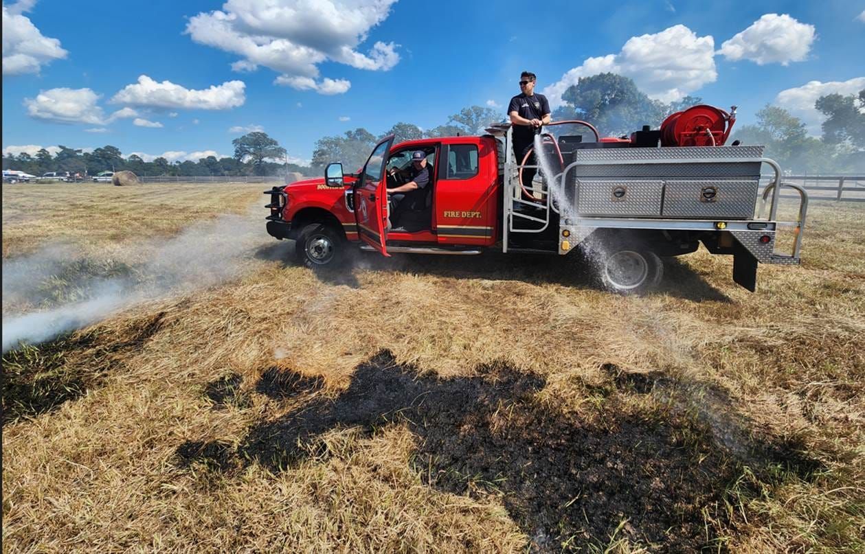 A red truck is spraying water on a field of dry grass.