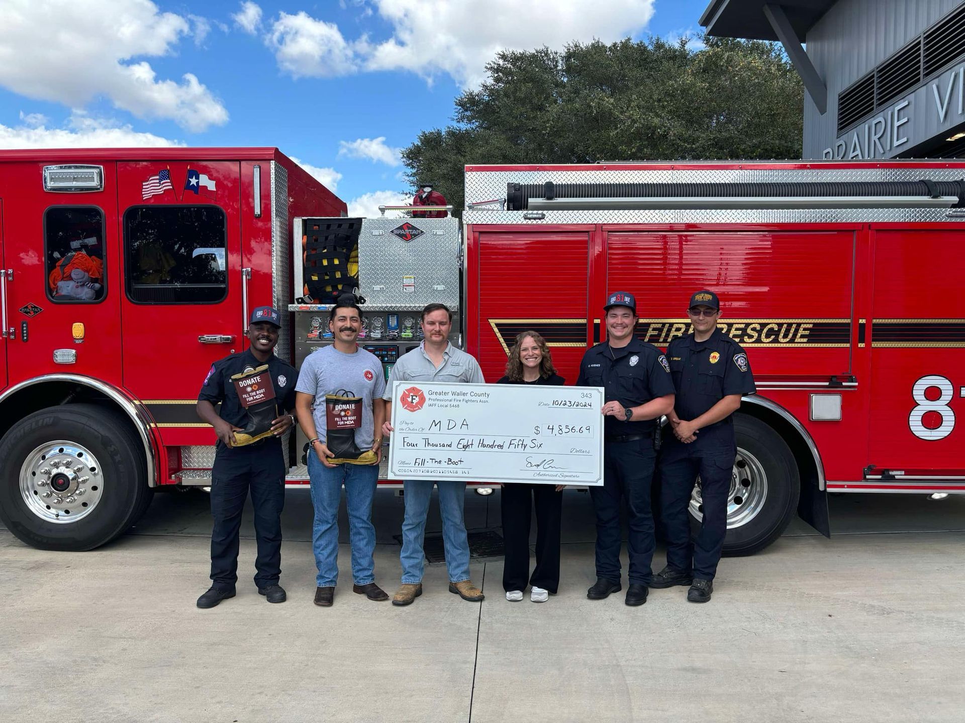 Group of emergency personnel with a large size check made payable to the Muscular Dystrophy Association.