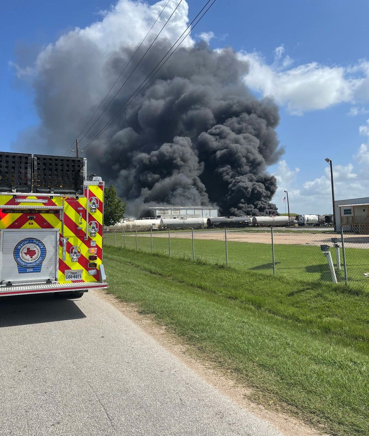 A fire truck is parked on the side of the road in front of a large smoke stack.