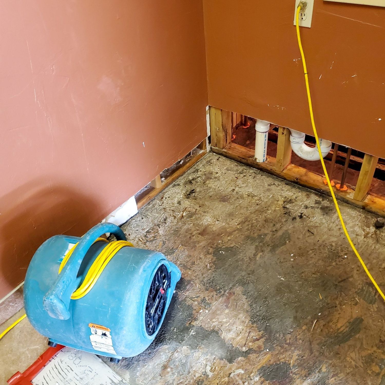 A blue dryer is sitting on the floor of a room next to a wall.