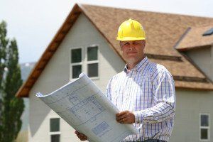 A man wearing a hard hat is holding a blueprint in front of a house.