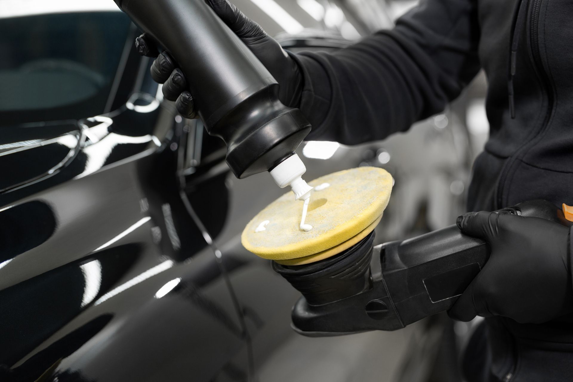 A person is polishing a black car with a machine.