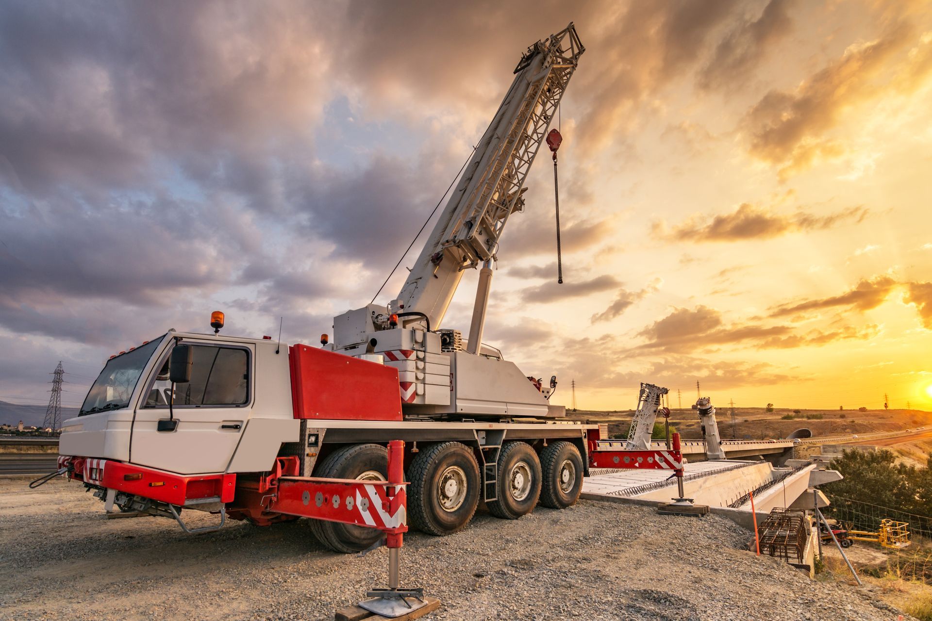 Red and white mobile crane parked on gravel at sunset near the waterfront